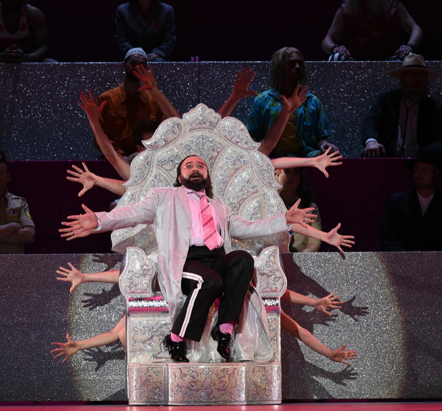 Ralf Rachbauer als Dr. Feel-Good in »Anna Nicole« am Staatstheater Wiesbaden: auf einem verzierten Thron, umgeben von Tänzerinnen und Tänzern